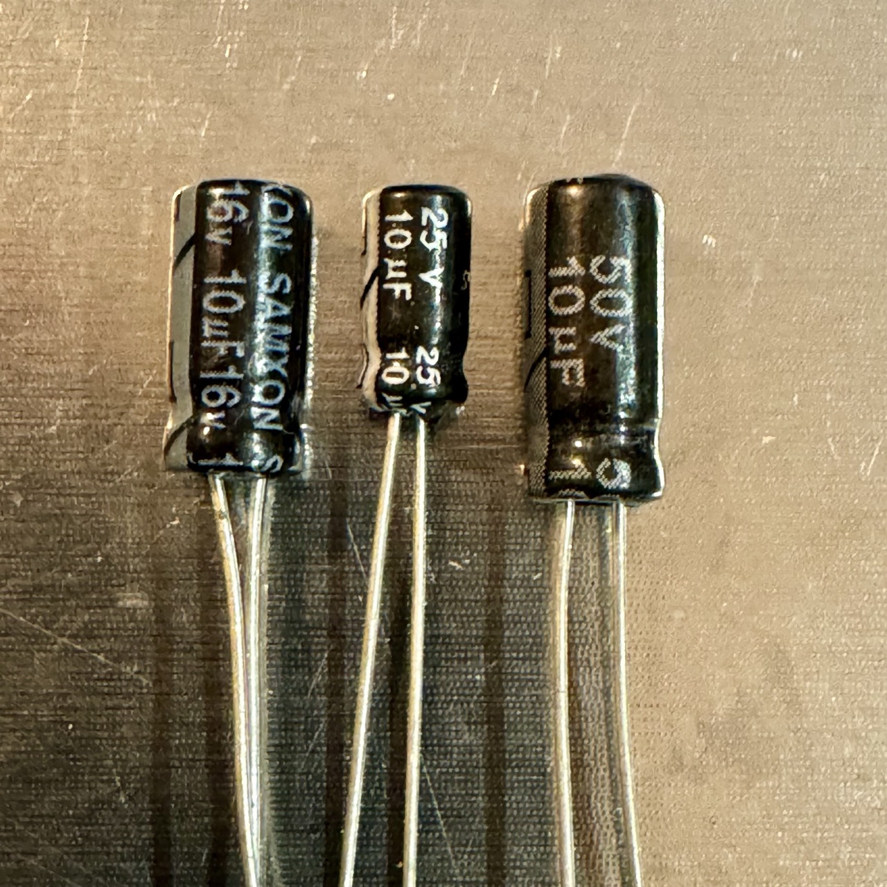 Size comparison of three 10uF electrolytic capacitors (16V, 25V, 50V) arranged from left to right